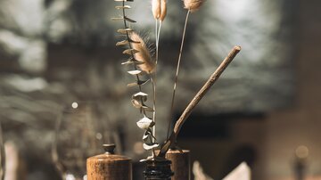 A stylish table decoration with a glass bottle and dried flowers. In the background, soft lighting conditions and additional table accessories are visible.
