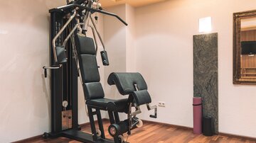A modern fitness machine stands in a room with a wooden floor. The walls are light-colored, and there are some decorative elements.