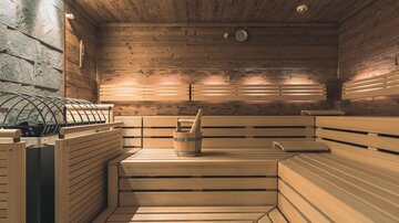 A modern sauna with wooden benches and soft lighting. A wooden container stands in the middle of the sauna.