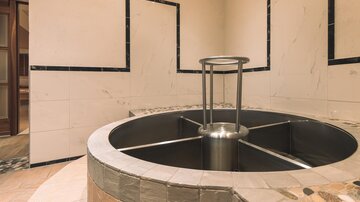 A modern wellness area with a round hot tub in the center. The walls are elegantly tiled, creating a calming atmosphere.