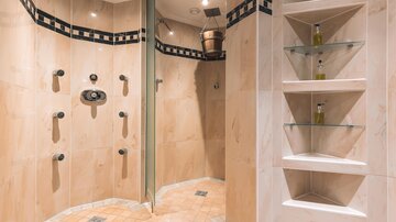 A modern shower area with multiple water jets and elegant furnishings. The walls are in neutral tones, and there is a shelf for personal care products.