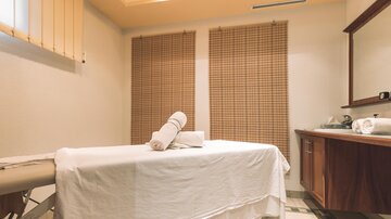 A relaxing massage room with a prepared table and fresh towels. The walls are neutral, and there are natural light sources.