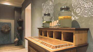 A modern tea station made of wood with two glass containers for flavored water. Stylish wall decorations can be seen in the background.