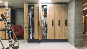 A modern ski cellar with wooden cabinets. The cabinets are open and display ski equipment, while a ski pole stands in the foreground.