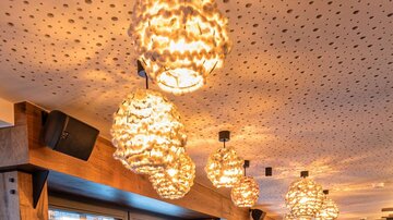 Ein gemütliches Restaurant mit Holzinterieur und modernen Lampen. Die Sitzecken sind mit kariertem Stoff und roten Stühlen ausgestattet.