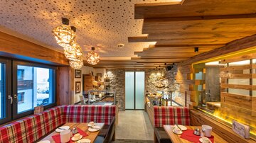 Ein gemütliches Restaurant mit hölzernen Wänden und modernen Lampen. Die Tische sind mit roten und weißen Tischdecken gedeckt und es gibt eine einladende Atmosphäre.