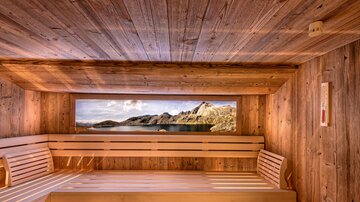 Eine gemütliche Sauna mit Holzverkleidung und Blick auf die Natur. Sanfte Lichtverhältnisse schaffen eine entspannende Atmosphäre.