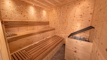 Eine gemütliche Sauna aus Holz mit Sitzbänken und sanfter Beleuchtung. Der Raum vermittelt Entspannung und Wohlbefinden.