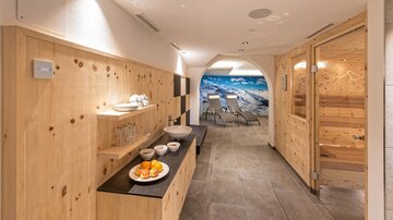 Ein helles Wellness-Bereich mit Holzverkleidung und einer Sauna. Im Hintergrund ist ein Strandbild zu sehen, das eine entspannende Atmosphäre schafft.