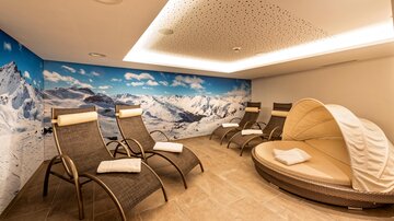 Ein entspannender Wellnessbereich mit mehreren Liegen und einer gemütlichen Rundliege. Die Wand ist mit einem Bild von schneebedeckten Bergen gestaltet.