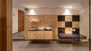Ein moderner Wellnessbereich mit Holzregalen und einer komfortablen Sitzgelegenheit. Die Beleuchtung sorgt für eine angenehme Atmosphäre.