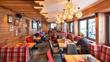 Ein gemütliches Restaurant mit Holzwänden und warmen Lichtquellen. Die Einrichtung ist rustikal, mit gepolsterten Sitzen und einem einladenden Ambiente.