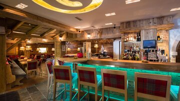 Eine gemütliche Bar mit rustikalem Holzinterieur und hellen Beleuchtungselementen. Der Barbereich ist modern gestaltet und lädt zum Verweilen ein.