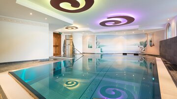 Ein eleganter Innenpool mit sanften, geschwungenen Mustern an der Decke. Warmes Licht schafft eine entspannende Atmosphäre.