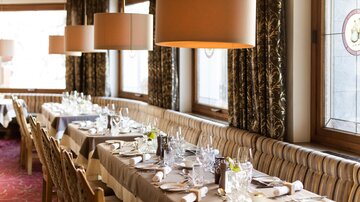 Ein elegantes Restaurant mit stilvoll gedeckten Tischen. Weiche Beleuchtung und Fenster sorgen für eine einladende Atmosphäre.