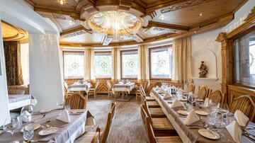 Ein elegantes Restaurant mit Holzdekor und großen Fenstern. Die Tische sind festlich gedeckt und laden zu einem gemütlichen Essen ein.