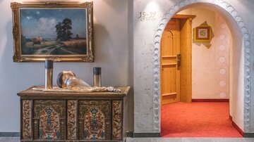 Eine stilvolle Lobby mit einem kunstvollen, bemalten Schrank und einem Gemälde an der Wand. Im Hintergrund führt ein gewölbter Durchgang zu einem Zimmer mit einer roten Teppichboden.