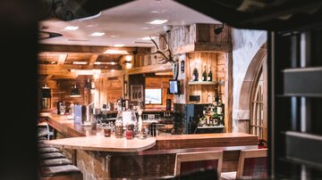 Eine gemütliche Bar mit Holzregalen und einer einladenden Theke. Flaschen und Getränke sind gut sichtbar auf dem Bartresen angeordnet.