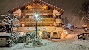 Ein schönes Hotel im Schnee, umgeben von einer winterlichen Landschaft. Die schneebedeckte Straße und die beleuchtete Fassaden verleihen eine gemütliche Atmosphäre.