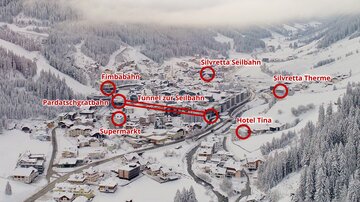 Ein verschneites Dorf in den Bergen mit verschiedenen Skiliften und einem Hotel. Die Umgebung ist idyllisch und von Bäumen und Bergen umgeben.