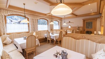 Eine gemütliche Restaurantumgebung mit Holzmöbeln und eleganten Tischdekorationen. Große Fenster lassen viel Tageslicht hinein und sorgen für eine einladende Atmosphäre.