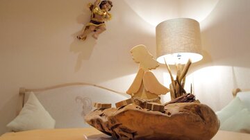 Ein gemütlicher Raum mit einer Holzskulptur und einem Lampenlicht. An der Wand hängt eine weitere Holzfigur.