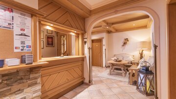 Ein einladender Empfangsbereich mit Holzvertäfelung und warmem Licht. Es gibt eine gemütliche Sitzecke und dekorative Elemente, die eine angenehme Atmosphäre schaffen.