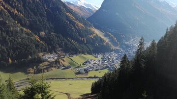 Eine malerische Berglandschaft mit einem kleinen Dorf im Tal. Hohe Berge und grüne Wiesen prägen die Umgebung.
