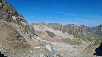 Eine beeindruckende Berglandschaft mit steilen Felsen und weiten Tälern. Der Himmel ist klar und blau, was die natürliche Schönheit der Umgebung hervorhebt.