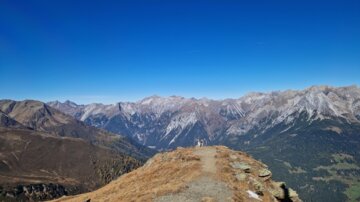 Eine beeindruckende Berglandschaft mit schneebedeckten Gipfeln und klarem blauen Himmel. Der Weg führt auf einen panoramischen Aussichtspunkt.