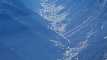 Ein beeindruckendes Bergtal mit grünen Wiesen und Häusern. Die umgebenden Berge sind majestätisch und unter einem klaren Himmel sichtbar.