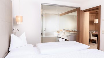 Ein modernes Hotelzimmer mit einem großen Bett und einem eleganten Badezimmer. Der Raum ist hell und freundlich gestaltet.