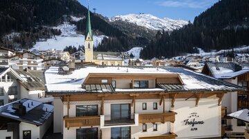 Ein charmantes Hotel in einer schneebedeckten Berglandschaft. Die beeindruckenden Berge und der Kirchturm verleihen der Szene eine malerische Note.