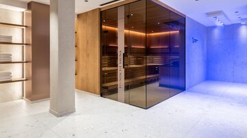 Eine moderne Sauna mit Glasfront und warmen Lichtern. Der Raum ist elegant gestaltet und bietet eine entspannende Atmosphäre.