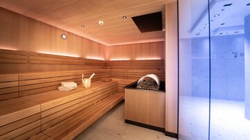 Eine moderne Sauna mit Holzverkleidung und sanfter Beleuchtung. Der Raum ist gemütlich und einladend.