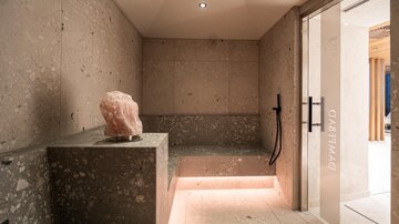 Ein modernes Dampfbad mit eleganten Steinwänden und sanfter Beleuchtung. Eine rosa Quarzskulptur dekoriert die Sitzfläche.