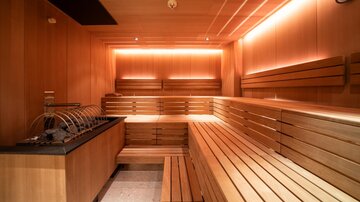 Eine moderne Sauna aus Holz mit sanfter Beleuchtung. Die Bänke sind ordentlich angeordnet und es gibt einen Platz für Getränke.
