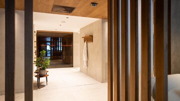 Ein moderner Empfangsbereich mit Holzelementen und sanften Farben. Eine Pflanze und ein Bademantel verleihen dem Raum einen einladenden Charakter.
