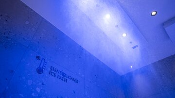 Ein moderner Raum mit blauen Lichtakzenten und einer Wand, die den Schriftzug "EISNIEBLGANG ICE PATH" zeigt. Es wirkt kühl und einladend.