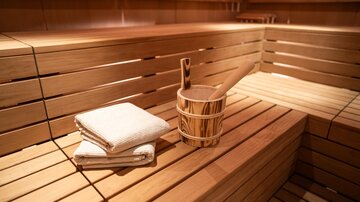 Eine gemütliche Sauna mit Holzbank und einem kleinen Eimer. Darin liegen zwei Handtücher bereit.