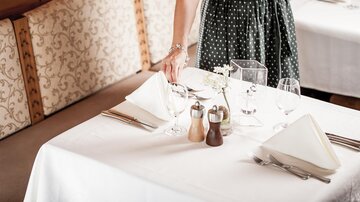 Ein elegant gedeckter Tisch in einem Restaurant. Eine Person bringt Geschirr und Glaswaren an den Tisch.