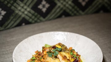 Ein ansprechend angerichteter Teller mit gebratenem Fisch und buntem Gemüse. Der Hintergrund zeigt ein elegantes Karomuster.