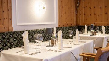 Ein elegantes Restaurant mit gedeckten Tischen und dekorativen Elemente aus Holz. Die Tischdecken sind weiß, und die Atmosphäre wirkt gemütlich und einladend.