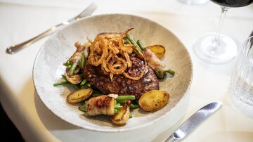 Ein köstliches Gericht mit gebratenem Fleisch, umgeben von grünen Bohnen und Kartoffeln. Dazu ein Glas Rotwein.