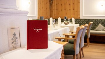 Ein elegantes Restaurant mit Holzvertäfelung und gedeckten Tischen. Im Vordergrund steht eine rote Speisekarte auf einem Tisch.