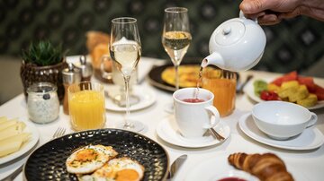 Ein stilvolles Frühstück mit Rühreiern, Croissant und frischem Obst. Im Hintergrund stehen Säfte und Gläser für Getränke.