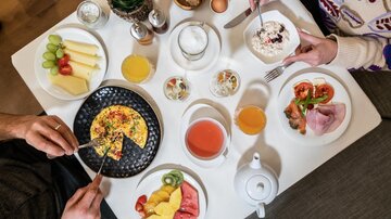 Ein reichhaltiges Frühstück auf einem Tisch mit verschiedenen Speisen. Darunter sind ein Omelett, frisches Obst, Aufschnitt und Getränke.