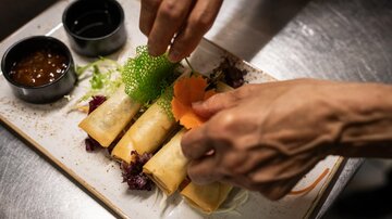 Ein Teller mit Frühlingsrollen wird dekoriert. Dazu gibt es zwei Dips und frisches Gemüse.