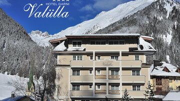 An elegant hotel in the mountains, surrounded by snow-covered fir trees. Clear blue skies and majestic mountains provide a picturesque backdrop.