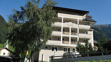 A modern building with several floors and balconies. Surrounded by trees and a mountainous landscape in the background.
